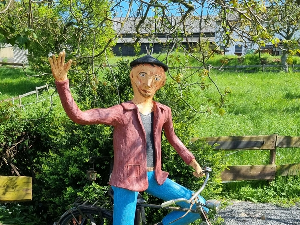 Eine Aufnahme von einer männlichen Figur die auf einem Fahrrad sitzt und winkt