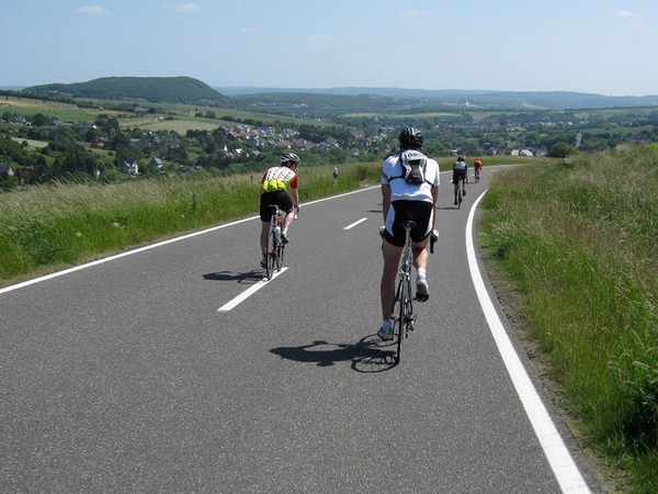 Mehrere Fahrradfahrer fahren eine Straße in der Natur entlang.