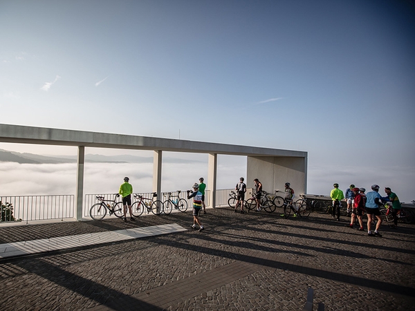 Mehrere Fahrradfahrer stehen auf einer Erhöhung und blicken in ein nebliges Tal.