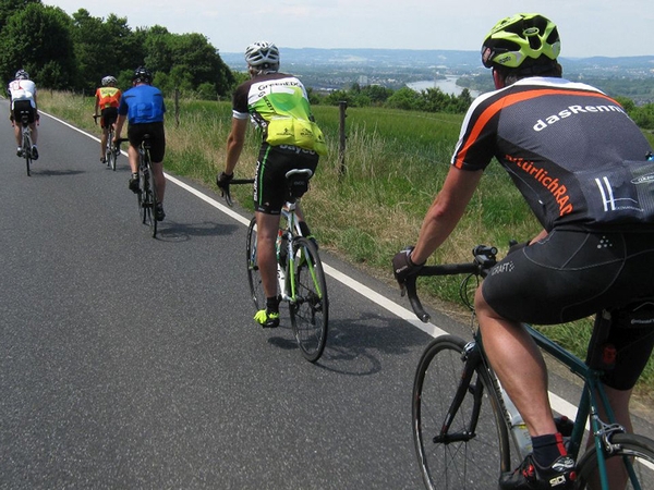 Mehrere Fahrradfahrer fahren eine Straße in der Natur entlang.