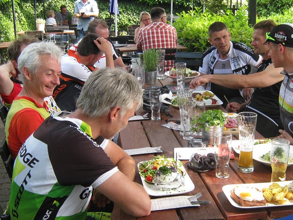 Mehrere Fahrradfahrer sitzen beim Essen an einem Tisch.