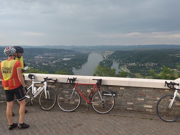 Mehrere Fahrradfahrer stehen auf einer Erhöhung und blicken auf den Rhein.