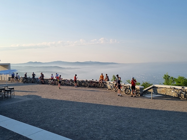 Mehrere Fahrradfahrer stehen an einer Mauer und blicken auf ein nebliges Tal.